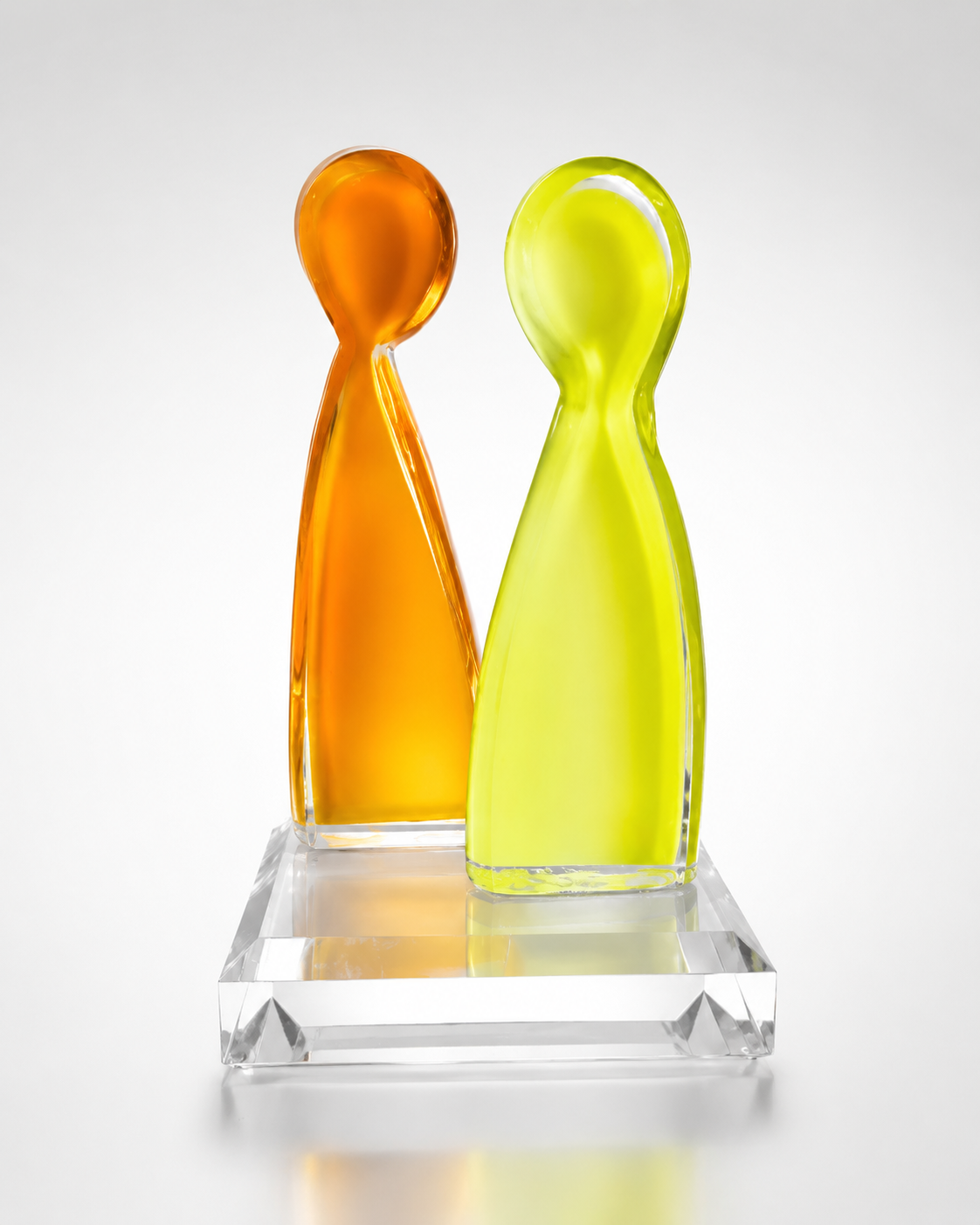 Two cast acrylic figurine sculptures in orange and yellow-green on a clear acrylic base